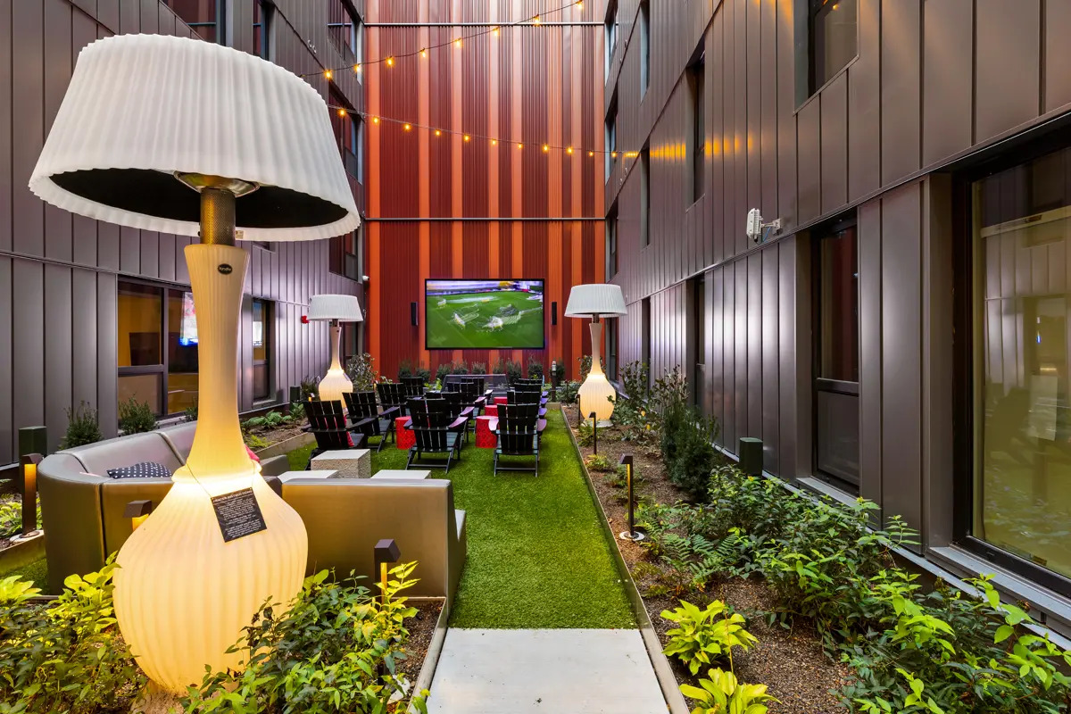 Greenspace courtyard with a large TV, artful lamps. and plantlife