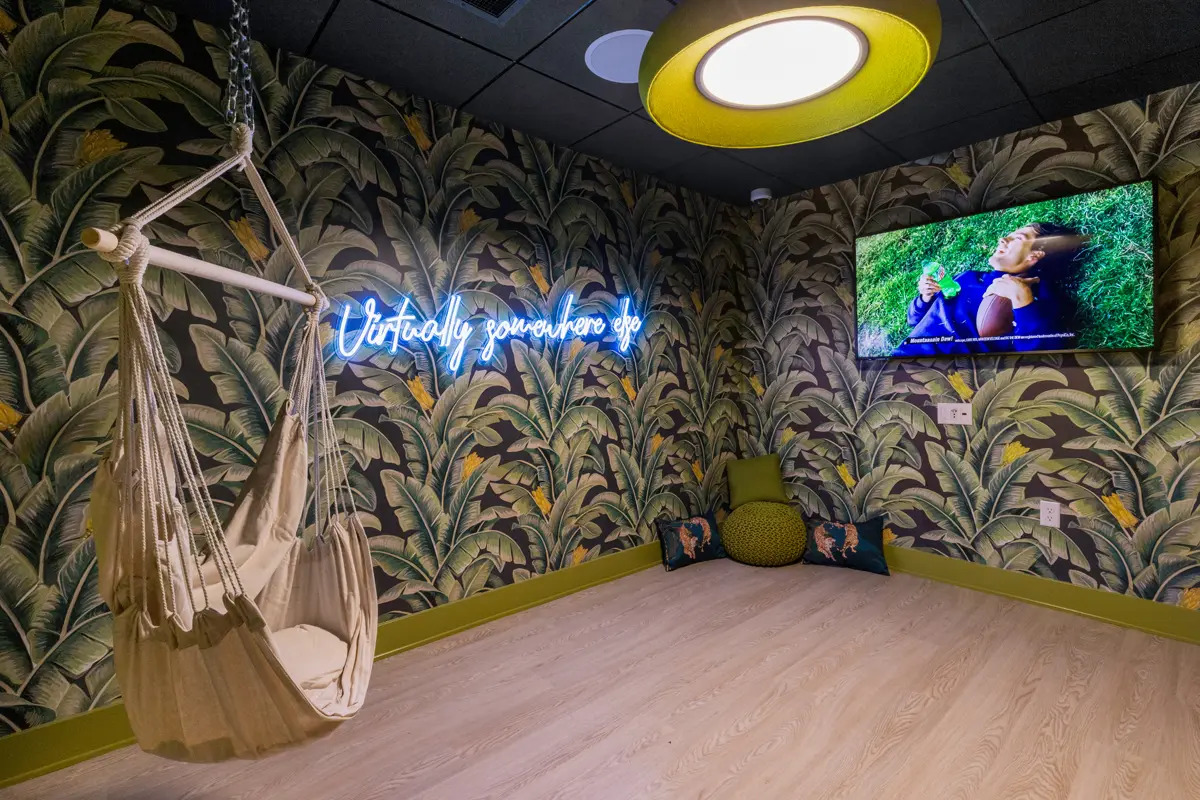 Hammock chair hangs in a jungle-themed room with a TV and a neon sign