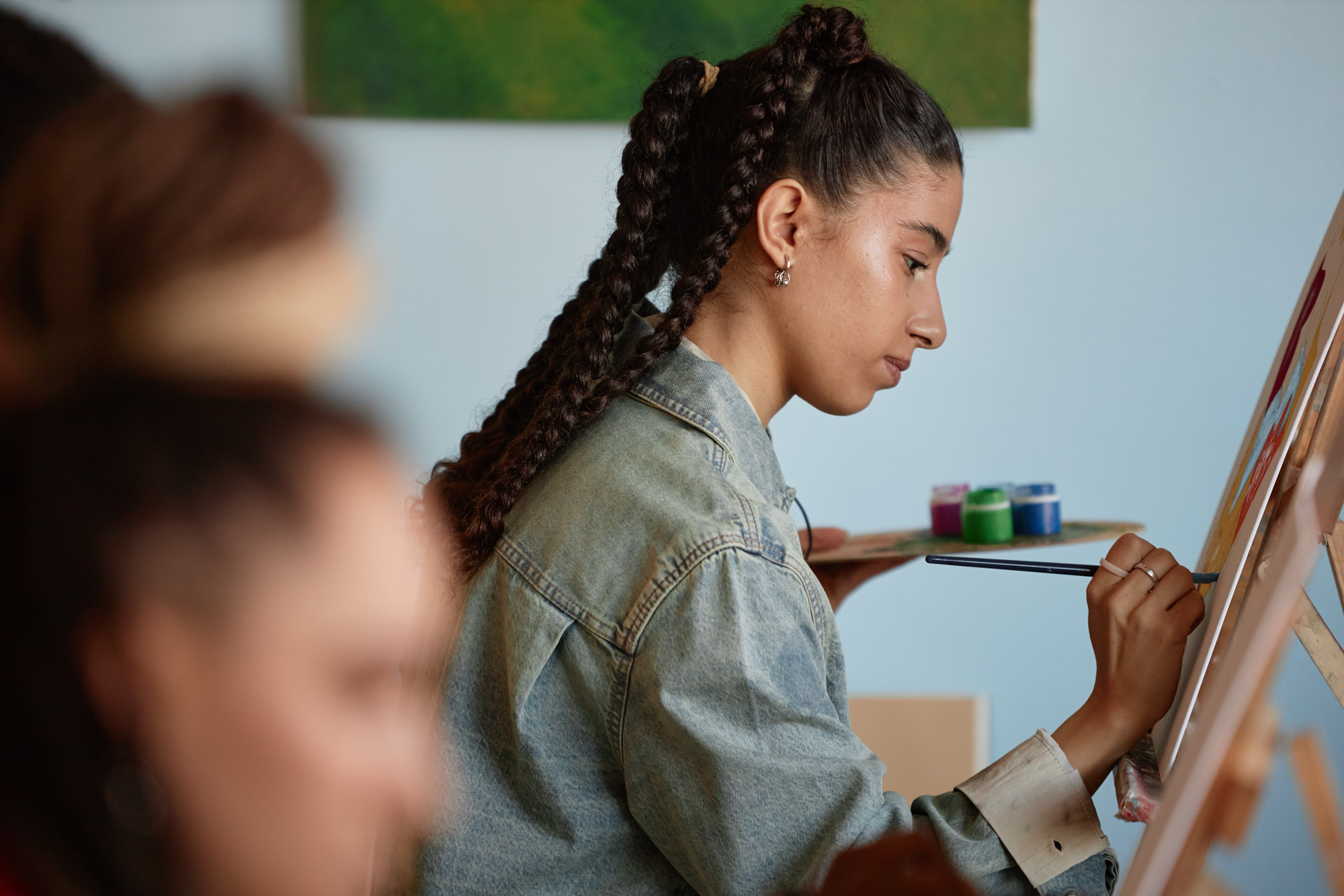 Young Adult Multicultural Woman Painting on Canvas during Art Class Indoors